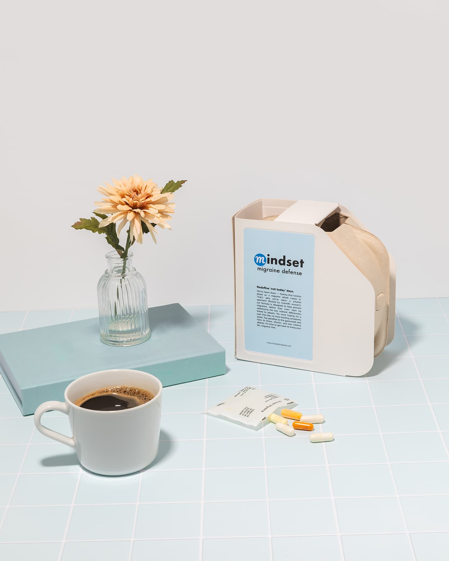 Mindset daily pack with single-day pouches, a mug of coffee, and a flower on a tiled surface